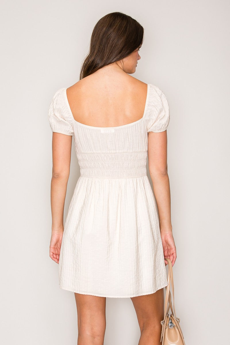 Cream textured square-neck front-tie-detail puff-sleeve smocked-waist babydoll mini dress - front full view showing square neckline, tie bow, puff sleeves, and smocked waist