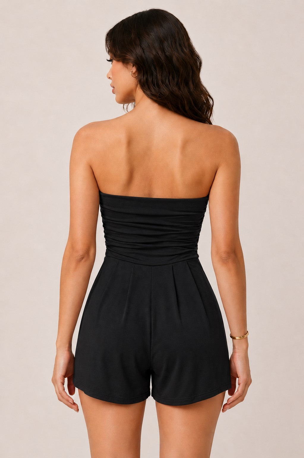 Black strapless ruched-tube-bodice pleated-shorts side-pocket romper - back view showing ruched tube bodice back, clean waistband, and pleated shorts from behind