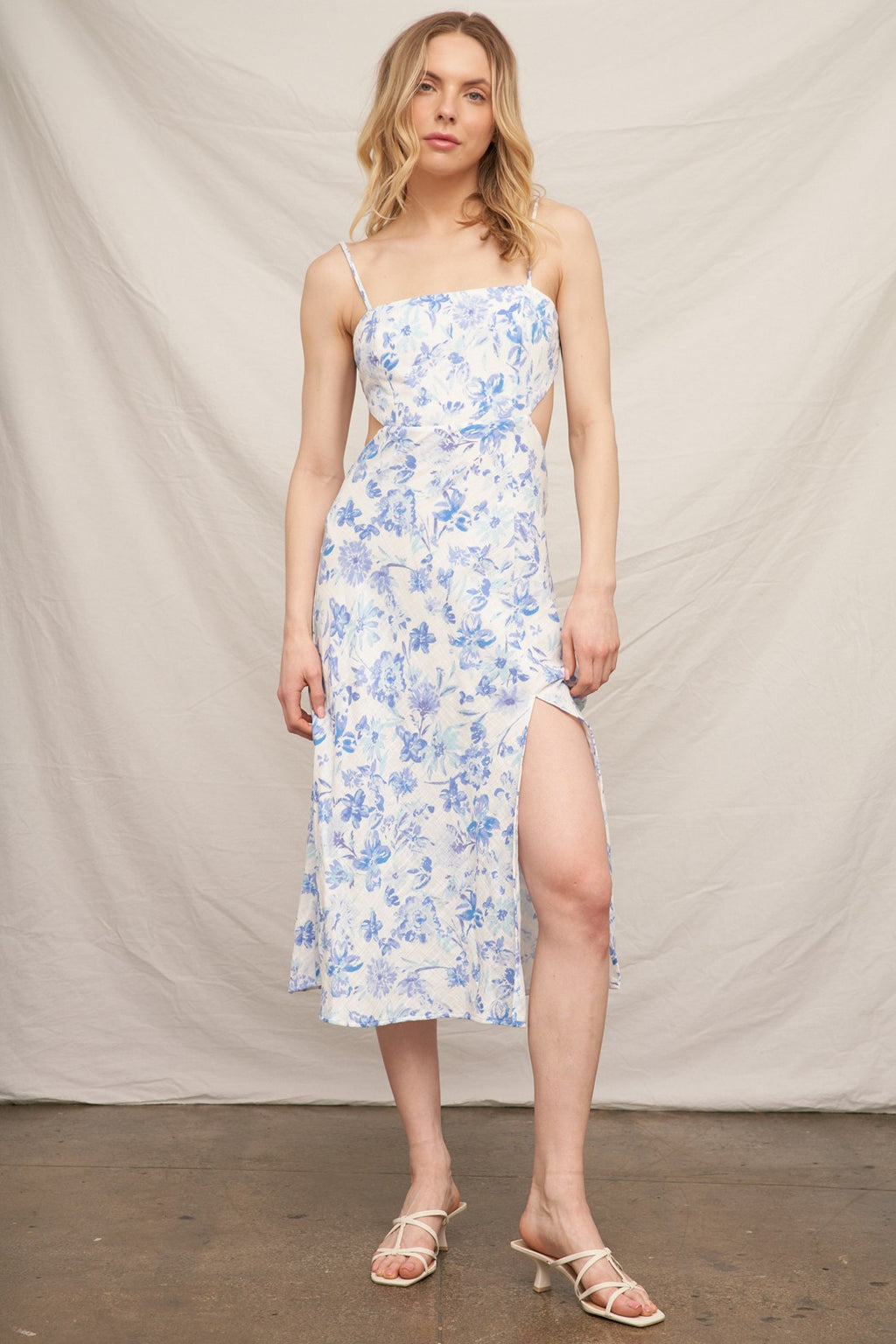 Blue floral spaghetti-strap square-neck side-cut-out back-bow-tie front-slit midi dress - front full view showing clean square neckline, fine spaghetti straps, fitted structured bodice, open side cut-outs at waist, fluid A-line midi skirt with front centre slit, and blue watercolour floral print on white