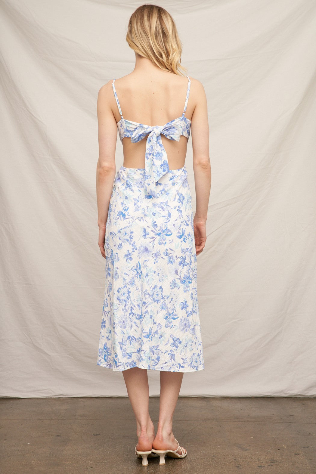 Blue floral spaghetti-strap square-neck side-cut-out back-bow-tie front-slit midi dress - back full view showing fine spaghetti straps, open back, large voluminous centre-back bow tie, and fluid A-line midi skirt from behind in blue watercolour floral on white