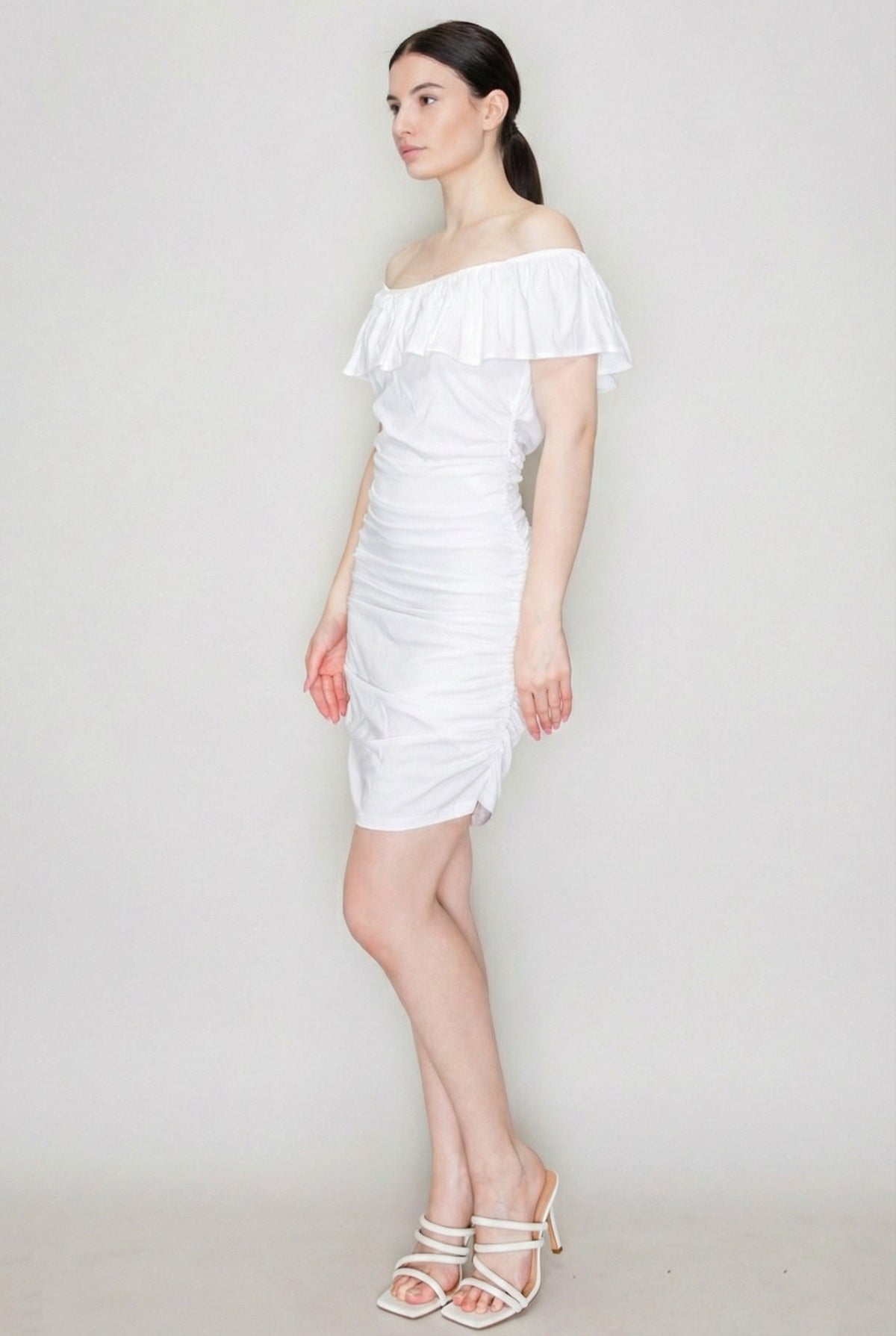 White off-shoulder ruffle-collar allover-ruched bodycon mini dress - side three-quarter view showing off-shoulder ruffle collar profile, ruched bodycon skirt silhouette, and mini length