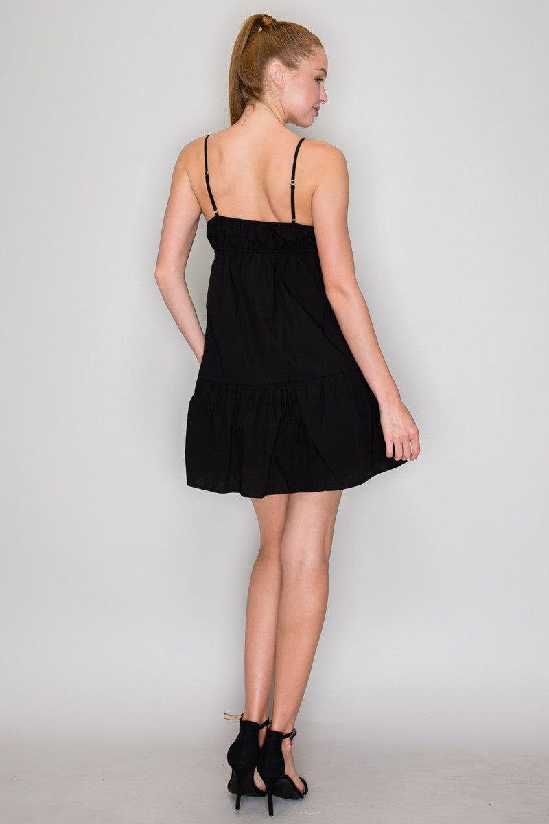 Black Swiss dot V-neck bow-front empire-waist tiered babydoll mini dress - side profile view showing gathered bust, empire bow, tiered babydoll skirt, and ruffle hem in black