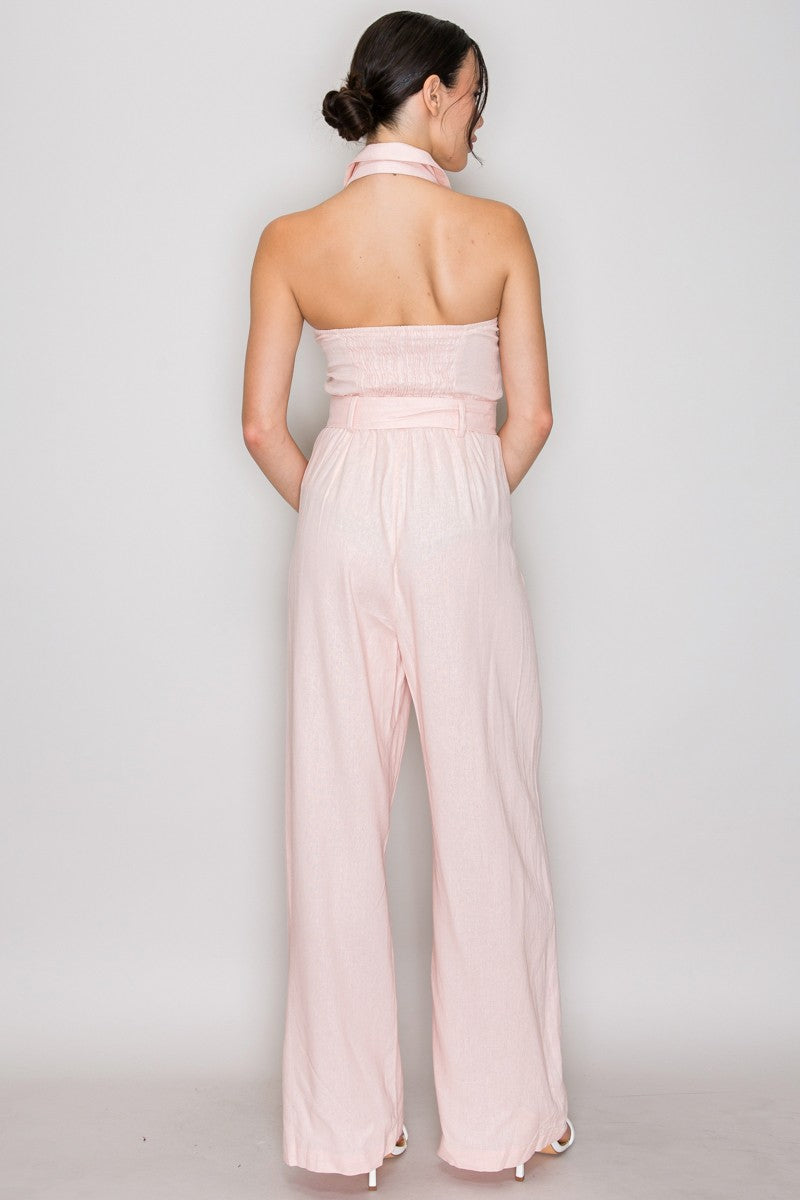 Natural linen halter-collar button-front belted wide-leg jumpsuit - front full view showing open shirt collar, halter neck tie, centre-front gold-tone metallic buttons, square-buckle belt at waist, and wide-leg trouser silhouette in natural linen