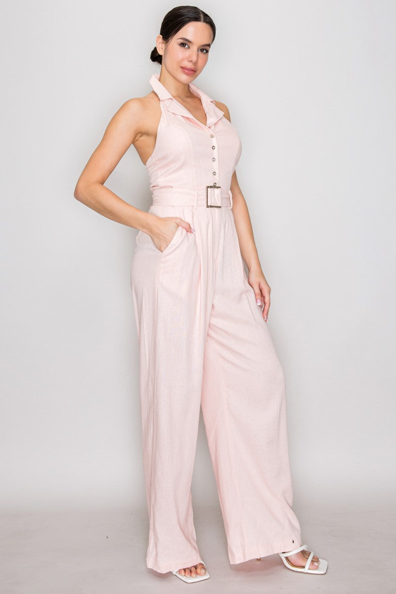 Natural linen halter-collar button-front belted wide-leg jumpsuit - back full view showing dramatic open back, halter neck tie at upper back, and wide-leg pleated trousers from behind in natural linen