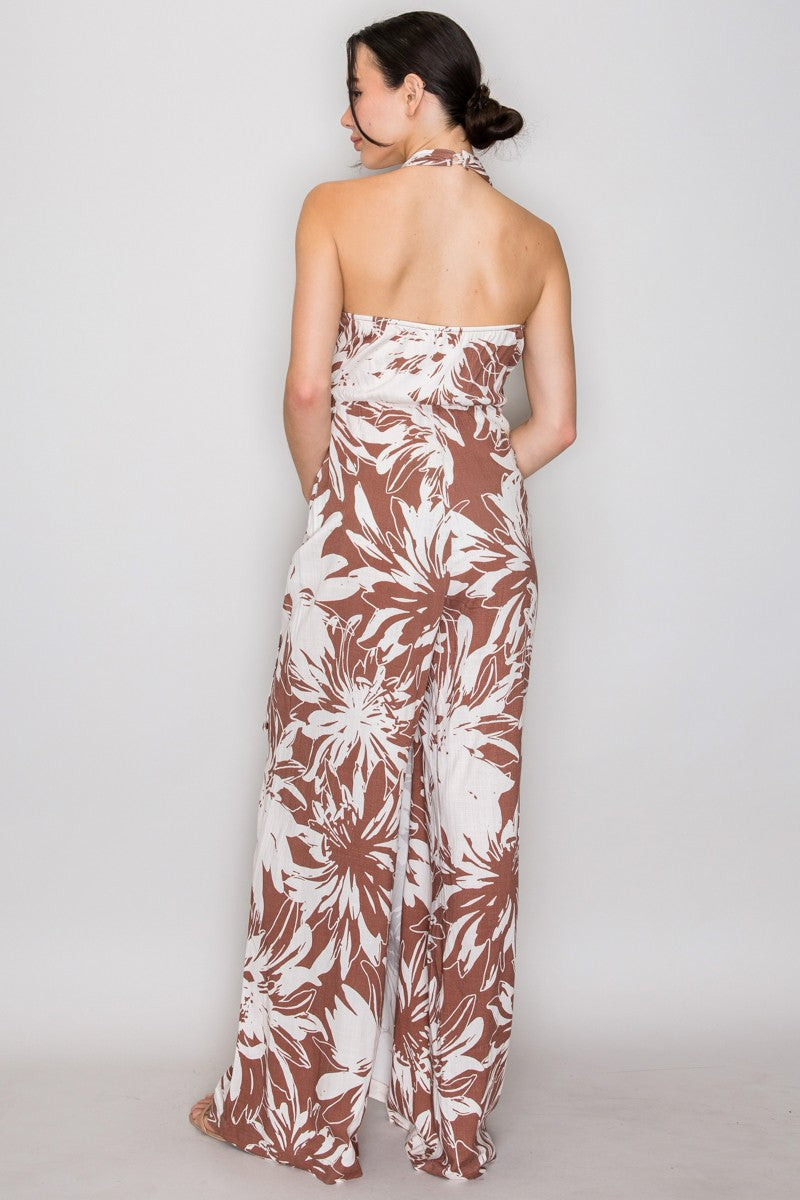 Mocha tropical floral halter deep-V wrap-bodice rattan-ring-buckle wide-leg jumpsuit - back full-length view showing halter neck tie at nape of neck, fully open bare back from neck to waist, and sweeping ultra-wide palazzo legs from behind in mocha and cream tropical floral print