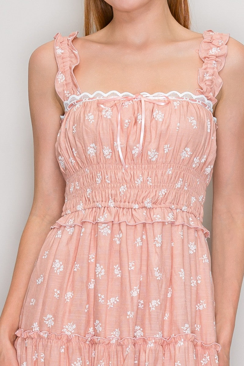 Blush ditsy-floral-print ruffle-strap scallop-lace-trim ribbon-tie smocked-bodice tiered midi dress - close-up front bodice detail showing ruffled strap edges, white scallop-edge lace neckline trim, tiny satin ribbon bow at centre-front, gathered bust, smocked waistband, and ruffled waist flounce in blush ditsy floral