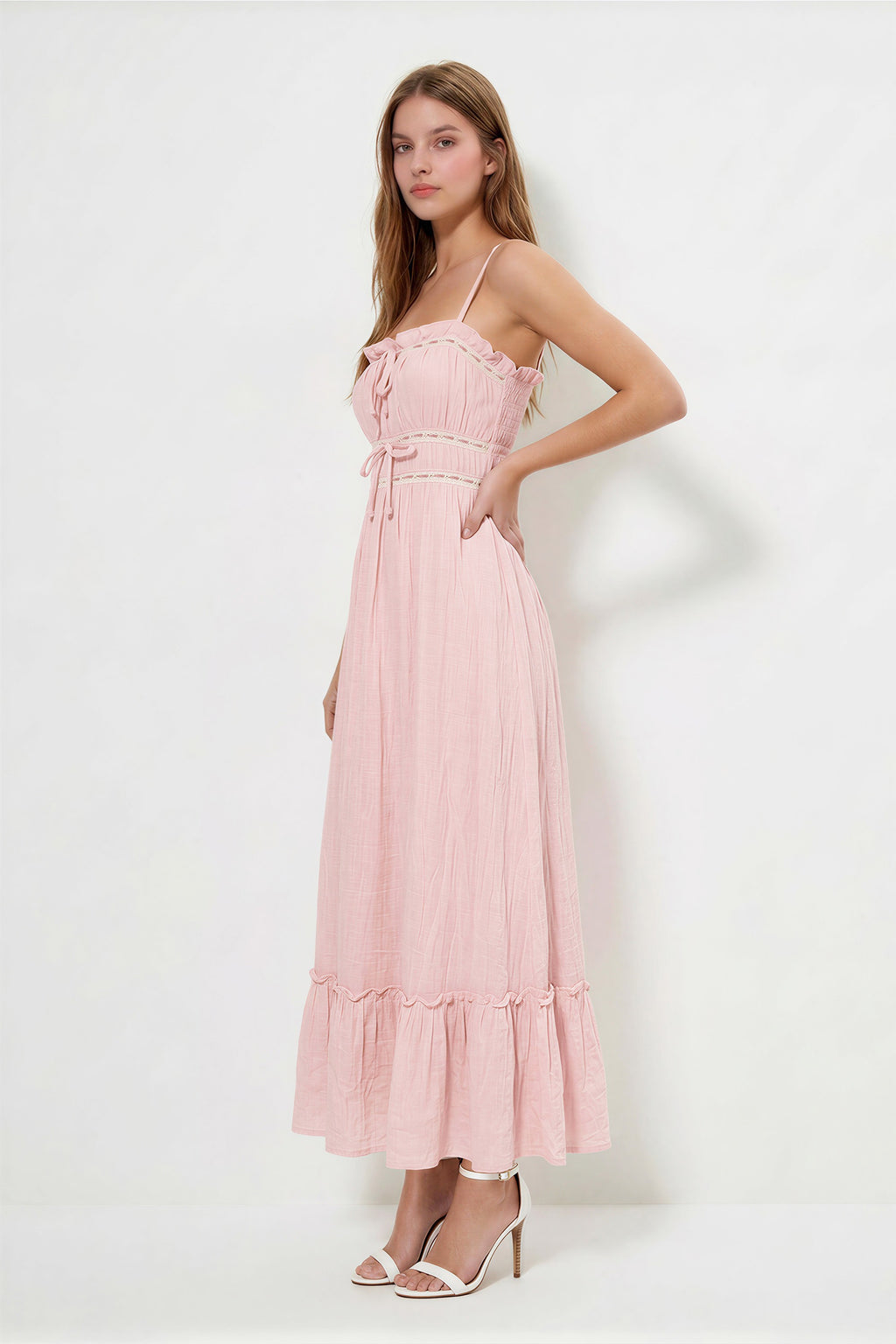 Blush spaghetti-strap ruffle-neckline crochet-lace-trim tie-front gathered-bodice ruffle-hem midi dress - side three-quarter view showing spaghetti straps, ruffle neckline, crochet lace trim bands, gathered bodice profile, pleated skirt, and ruffle hem from the side in soft blush pink