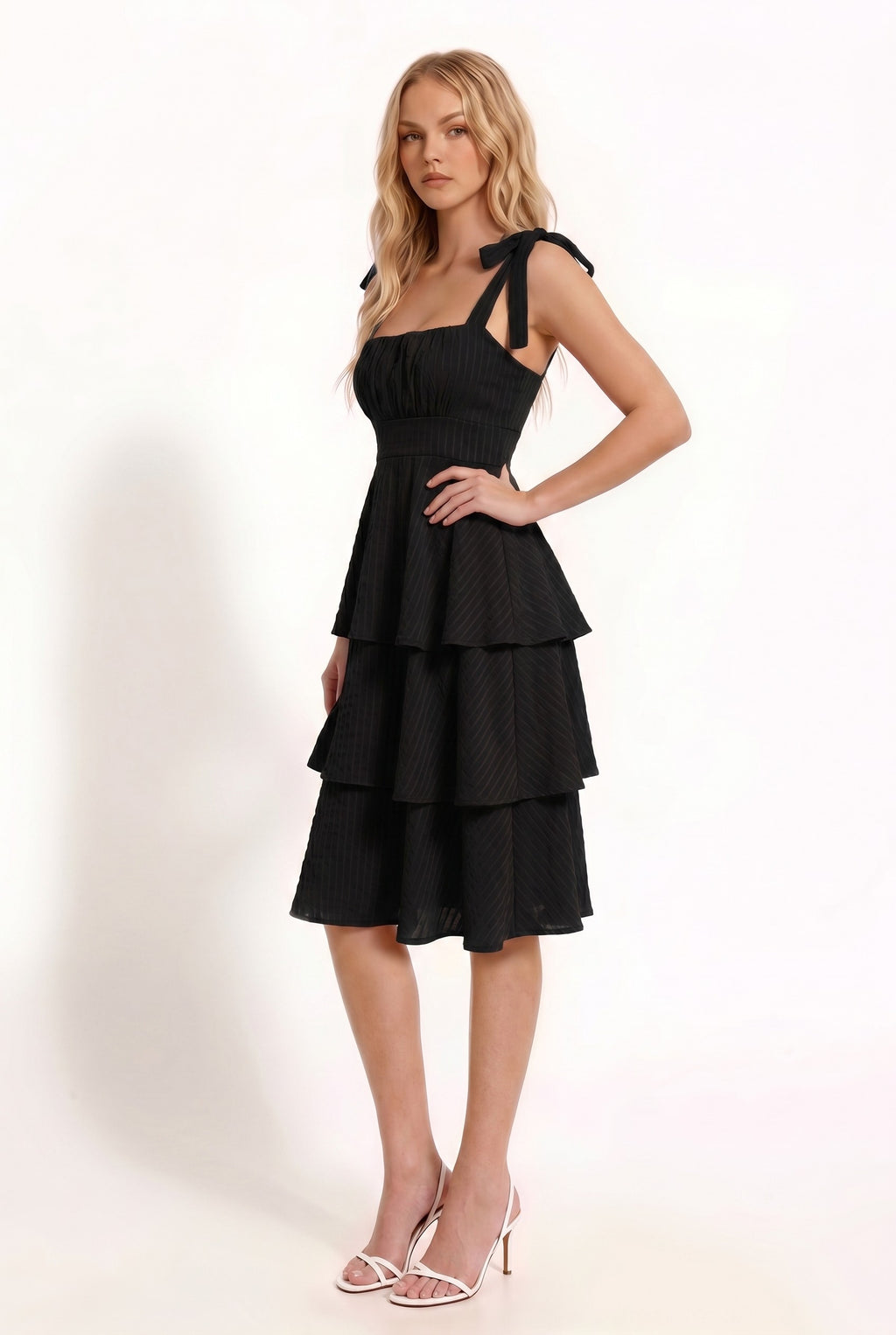 Black shoulder-tie-strap ruched-bust smocked-waist three-tier midi dress - close-up front bodice detail showing wide straps with self-tie shoulder bows, softly ruched gathered bust panel, and structured smocked waistband in deep black crinkle fabric