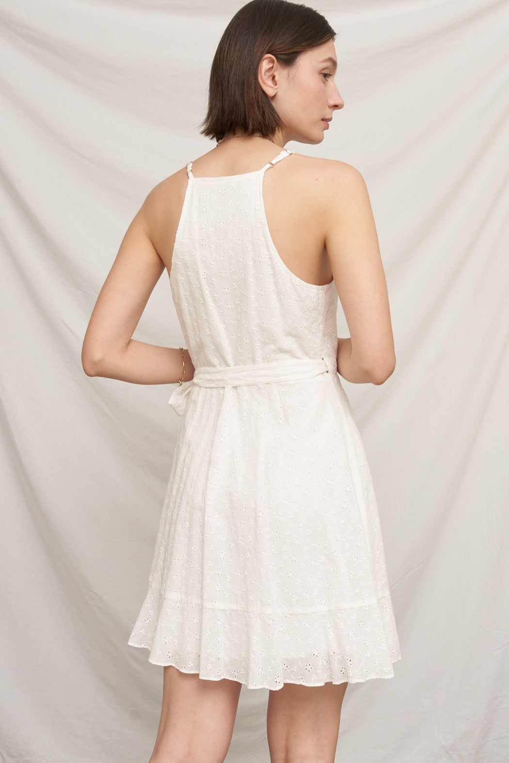 White eyelet spaghetti-strap V-neck ruffle-wrap tie-waist mini dress - back view showing cross-back X spaghetti straps, open back, waist tie, and flared eyelet skirt from behind