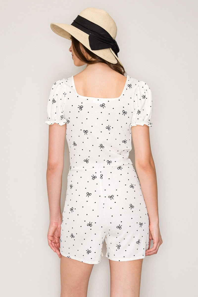 White bow-and-polka-dot-print deep-V puff-sleeve lettuce-edge button-front short romper - back view showing wide square back neckline, puff sleeves, and bow-polka-dot print