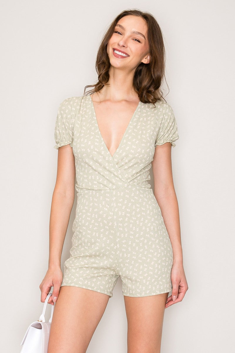 Cream ditsy-floral deep-V surplice puff-sleeve lettuce-edge smocked-waist short romper - front full view showing surplice V neckline, smocked waist, and shorts